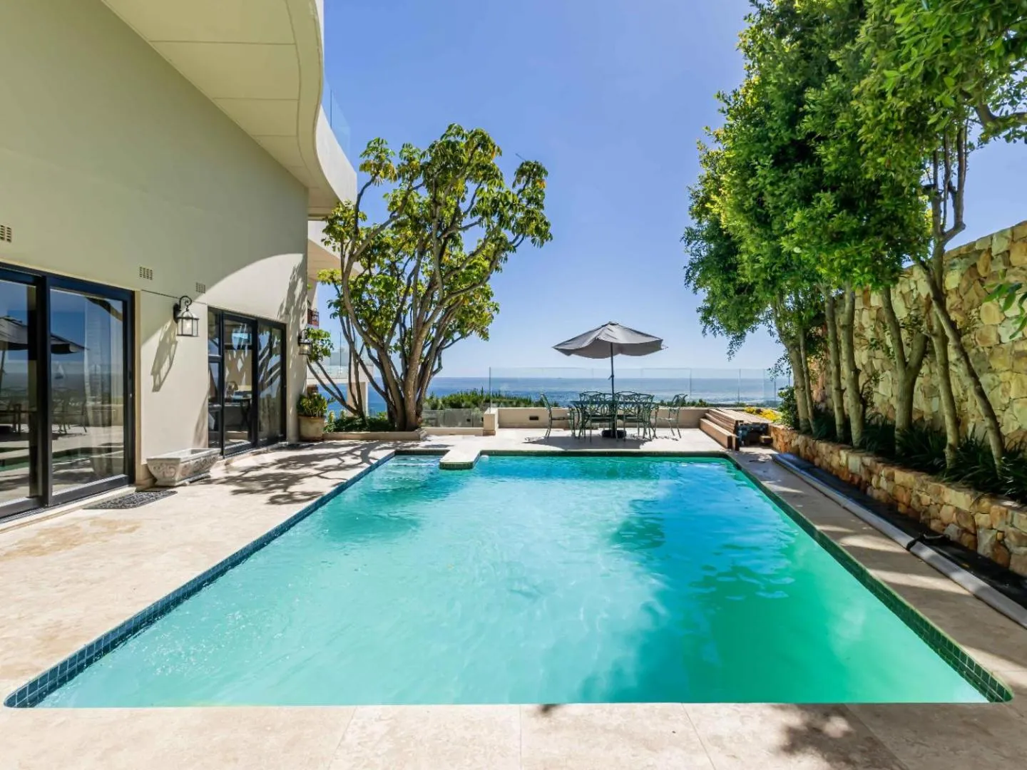 Pool with a parasol and mature trees above the sea