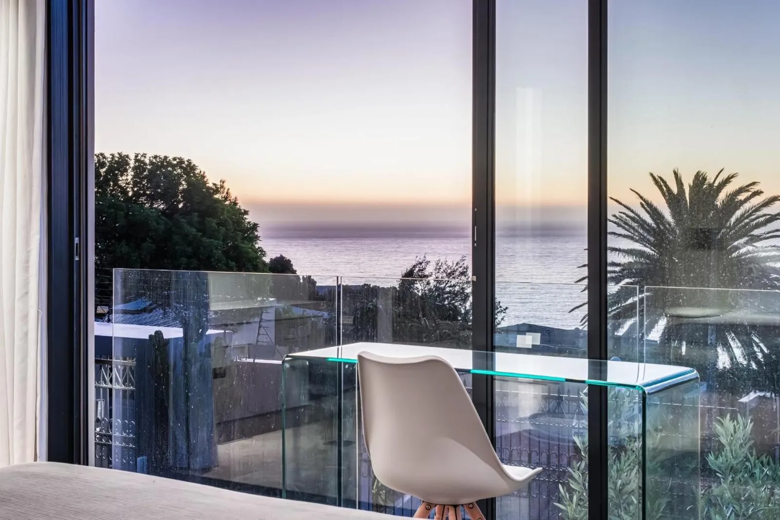 Floor-to-ceiling glass opening onto the sunset sea